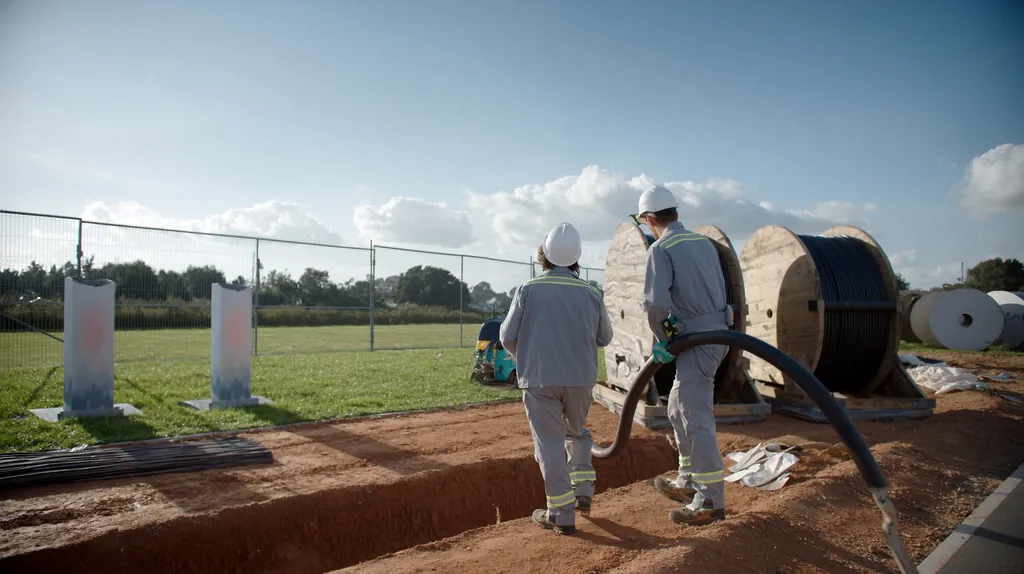 Zwei Monteure verlegen Stromkabel in einem Graben auf der Baustelle eines Ladeparks