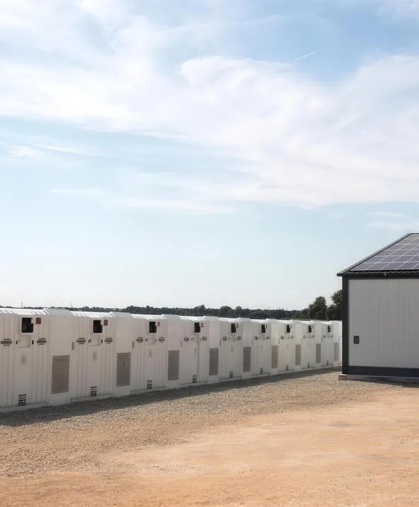 Weiße Batteriespeicher-Container neben einer Industriehalle mit Solardach